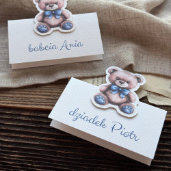 Stojąca personalizowana winietka urodzinowa Lazuro II z misiem z niebieską kokardą i imieniem gościa.