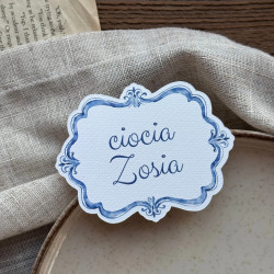 Personalizowana leżąca winietka urodzinowa Lazuro I z niebieską ramką i imieniem gościa.