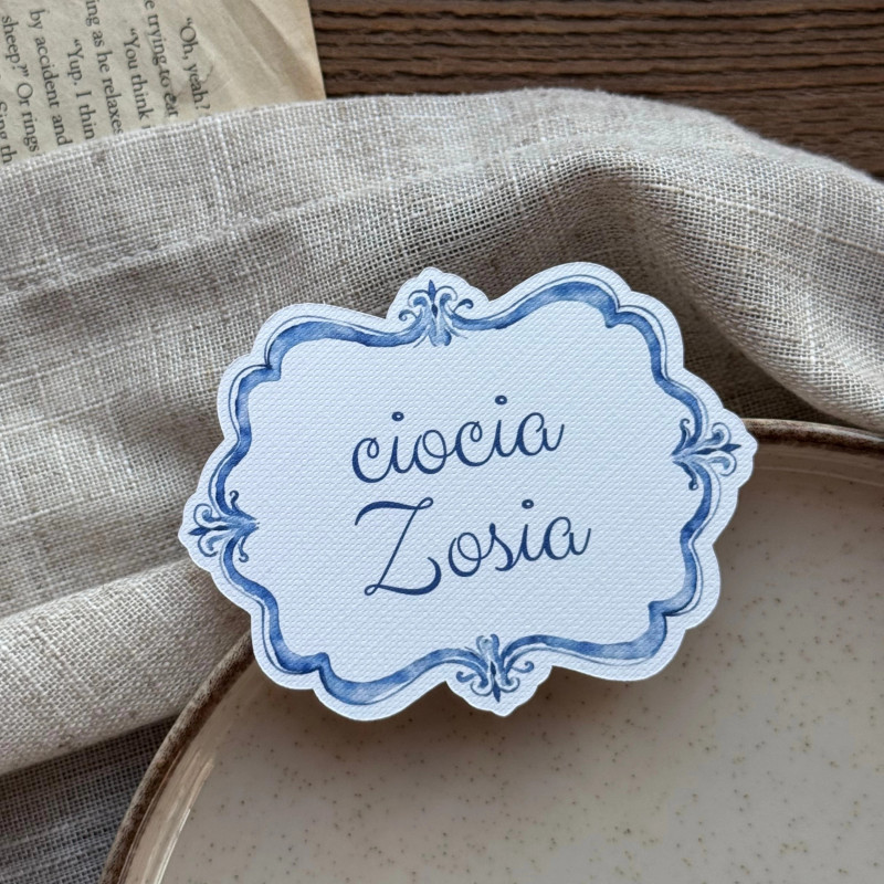 Personalizowana leżąca winietka urodzinowa Lazuro I z niebieską ramką i imieniem gościa.