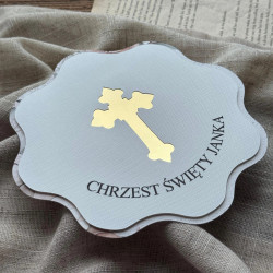 Zbliżenie na zaproszenie z okazji chrztu z wyciętym krzyżem podklejonym złotym lustrem.