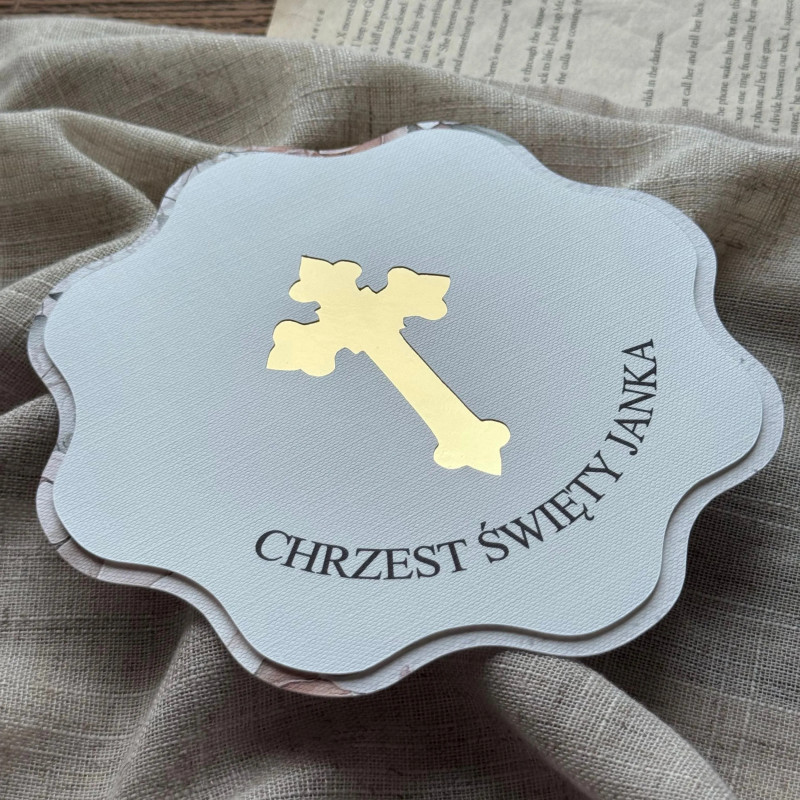Zbliżenie na zaproszenie z okazji chrztu z wyciętym krzyżem podklejonym złotym lustrem.