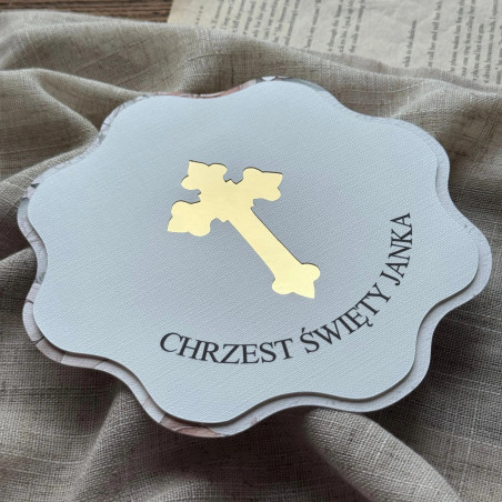 Zbliżenie na zaproszenie z okazji chrztu z wyciętym krzyżem podklejonym złotym lustrem.